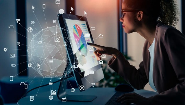 A woman touching a desktop screen that shows charts, surrounded by a network of connected icons