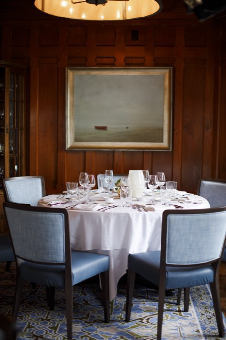 A round table set for six beneath the dining room's gilt-framed seascape.